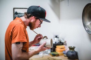 Man holding ceramic mug and applying glaze with paintbrush